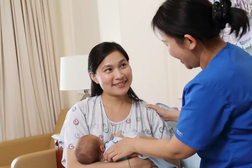 Smiling nurse providing support to a mother holding her newborn baby in a cosy hospital room