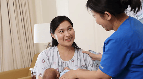 Smiling nurse providing support to a mother holding her newborn baby in a cosy hospital room